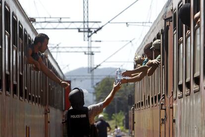 Un oficial de policía pasa una botella a los inmigrantes que emprenden el viaje en tren hacia Serbia, en la estación macedonia de Gevgelija. Solo en julio 107.500 personas (principalmente de Siria, Afganistán, Eritrea, Irak y Sudán del sur) han atravesado el Mediterráneo para alcanzar territorio europeo, según Frontex.