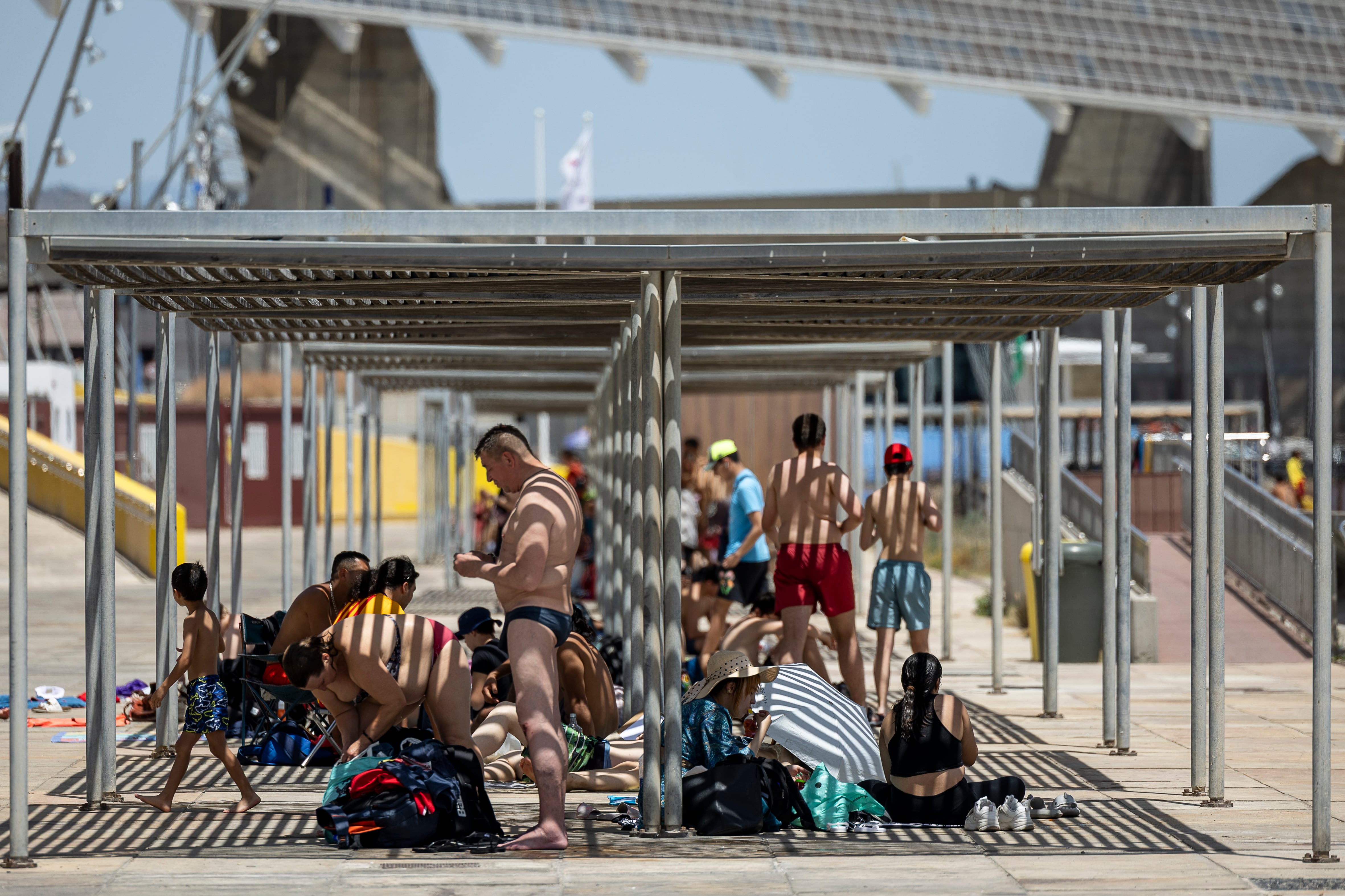 Varias personas intentan protegerse del sol bajo una pérgola de la zona del Fòrum de Barcelona durante la ola de calor.