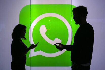 Duas pessoas usam seus celulares em frente ao logo do WhatsApp em Londres.