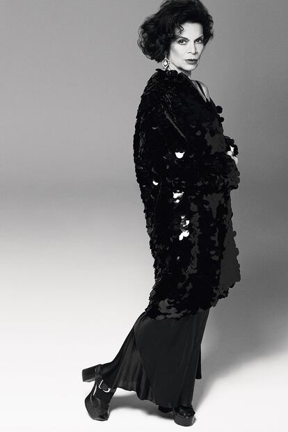 Bianca Jagger con abrigo de ‘paillettes’ negros de PRADA; vestido de seda negra de LA PERLA; zapatos de PRADA; pendiente con diamante de MIU MIU; medias de WOLFORD.