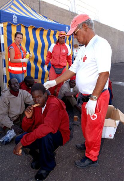Miembros de la Cruz Roja atienden, en el muelle de Arguineguín, a tres de los sesenta inmigrantes africanos que fueron rescatados en un cayuco.