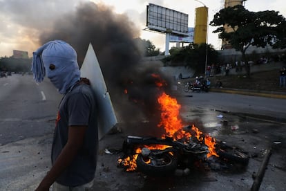 Un manifestante pasa por delante de una moto ardiendo durante una nueva jornada de protestas en Caracas.