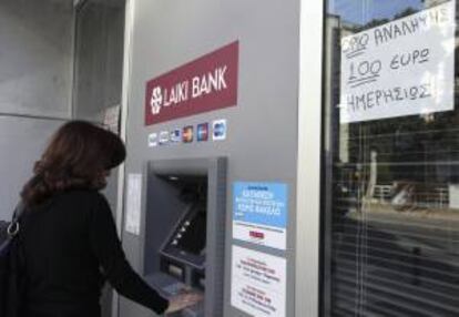 Una mujer usa el cajero automático de una sucursal del banco Laiki, con un cartel que informa de un límite de 100 euros de retirada de efectivo, ayer en Nicosia, Chipre.