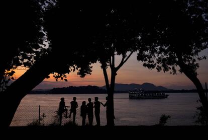 Un grupo de personas habla a la orilla del río Brahmaputra mientras un pequeño crucero navega en la localidad india de Gauhati.