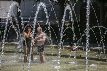 Dos personas se mojan en las fuentes de Madrid Río, este sábado. Este aire caliente, unido a la fuerte insolación diurna, el tiempo anticiclónico y a la baja térmica en el sur, sitúan las temperaturas por encima de los 40 grados en más de la mitad del país.