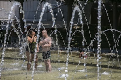 Dos personas se mojan en las fuentes de Madrid Río, este sábado. Este aire caliente, unido a la fuerte insolación diurna, el tiempo anticiclónico y a la baja térmica en el sur, sitúan las temperaturas por encima de los 40 grados en más de la mitad del país.