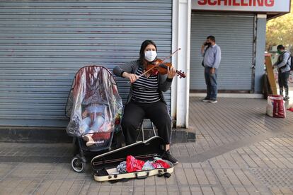 Mulher toca violino ao lado de seu bebê em uma rua de um setor comercial da capital.