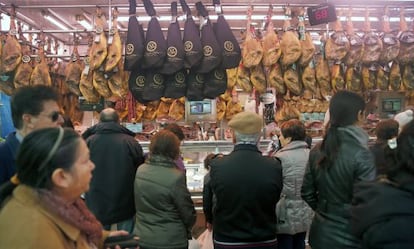 Diverses persones davant d'una parada de pernils al mercat central.