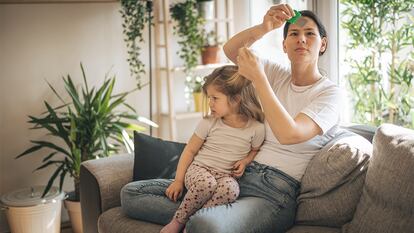 una madre mirando un peine antipiojos mientras su hija est encima dejndose quitar los piojos.