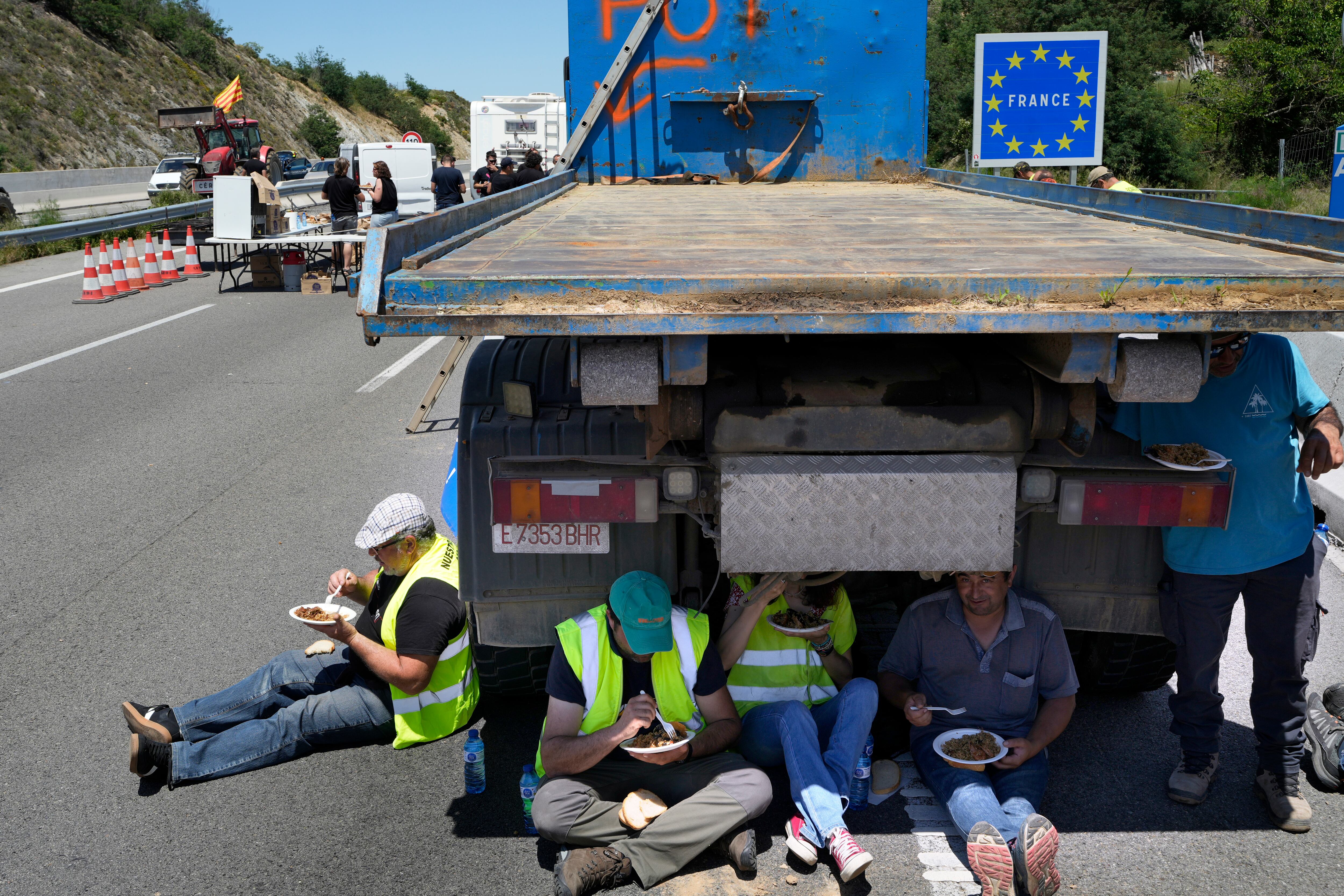 Varias personas descansan bajo un vehículo, mientras la AP-7 se encuentra completamente cerrada al tráfico en dirección a Francia por las protestas convocadas este lunes.