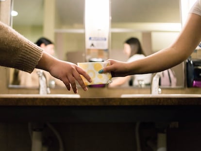 Uma pessoa entrega um absorvente a outra num ambiente escolar.