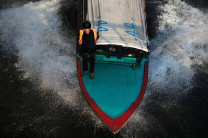 Un trabajador viaja a bordo de un barco por un canal en Bangkok (Tailandia).