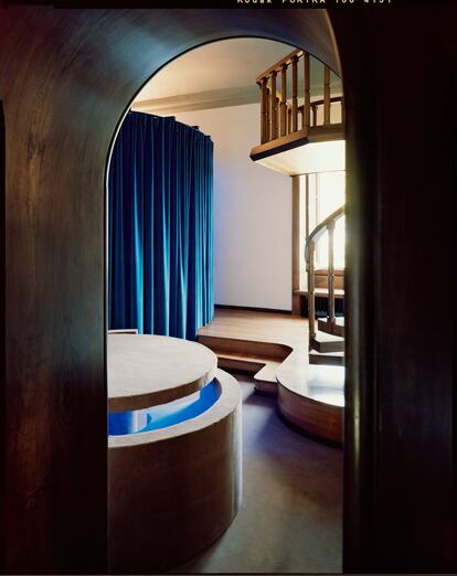 La moqueta beis recubre la mesa y el banco del comedor, el sofá y el dormitorio, en contraste con las cortinas azules.