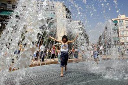 Una niña combate el calor al pasar bajo los surtidores de la fuente de la renovada Plaza de Manila de Alicante.