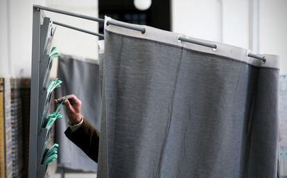 Detalle de un hombre cogiendo su papeleta en el interior de una cabina instalada en un colegio electoral de Triana, Sevilla