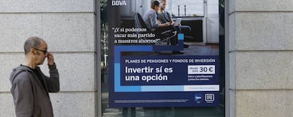 Una persona pasa delante de una oficina de BBVA donde se promocionan planes de pensiones.