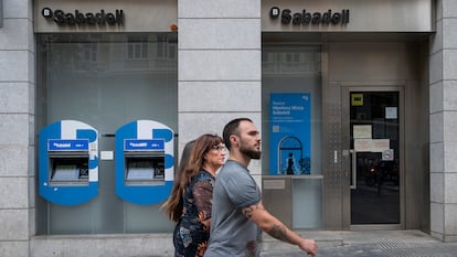 Tres personas pasan por delante de una sucursal de Sabadell.