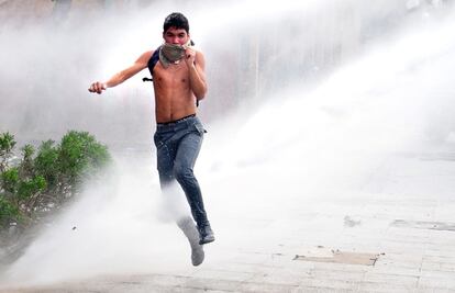 Un joven escapa de un chorro de agua lanzado por un vehículo de la policía chilena en la protesta del 28 de agosto.