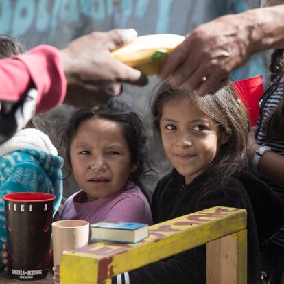 Dos niñas mexicanas hacen fila para conseguir su merienda, compuesta de plátanos y pan.
