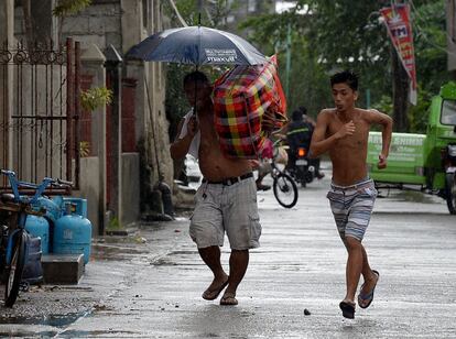 Un hombre transporta sus pertenencias a un lugar seguro mientras otro corre a cubrirse de las primeras lluvias causadas por el tifón, en la ciudad de Tuguegarao, Manila.