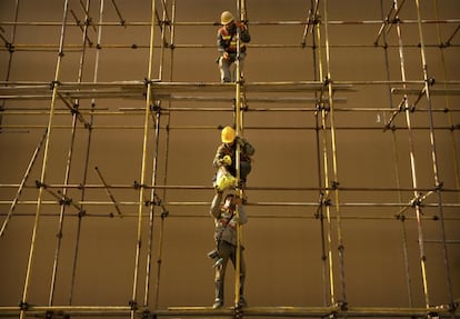 Trabajadores de la construcción se pasan una bolsa en el andamio de un centro comercial en Pekín, China.