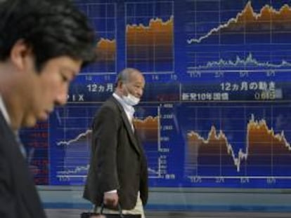 Dos hombres caminan junto a una pantalla informativa que muestra información bursátil en Tokio (Japón). EFE/Archivo