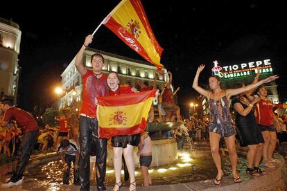 Unos aficionados ondean banderas de España tras bañarse en la fuente de la Puerta del Sol de Madrid.