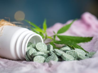 Green medical tablet pills with infused cannabis oil and marijuana leaves closeup