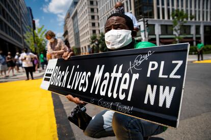 Un hombre sostiene un letrero con el nuevo nombre de la calle 16:  plaza Black Lives Matter.