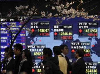 Varias personas caminan junto a un panel que muestra la información de la bolsa en Tokio. EFE/Archivo