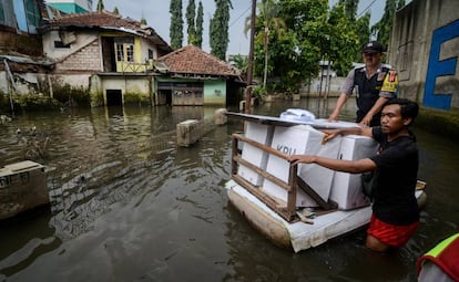 Los funcionarios transportan los materiales electorales en una balsa para distribuirlos en un área inundada en Bandung, provincia de Java Occidental (Indonesia).