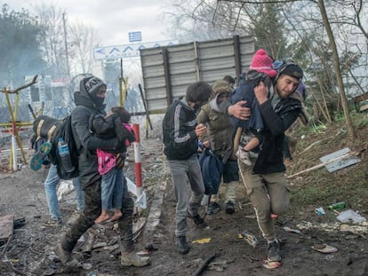 Unos padres protegen a sus hijos de los botes lacrimógenos lanzados por la policía griega, este sábado en Pazarkule.