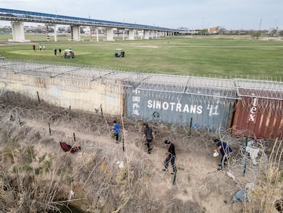 Migrants walk on the banks of the Rio Grande river to find a way to enter the U.S. as golfers play on the other side of the shipping container fence in Eagle Pass, Texas, U.S., February 27, 2024.