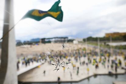 Manifestantes partidarios de Bolsonaro, en la explanada donde se encuentra el Congreso, vistos a través de una ventana rota.
