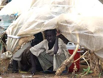 Un niño se refugia bajo un plástico para protegerse de la fuerte lluvia que caía en el campo de refugiados de Otash.