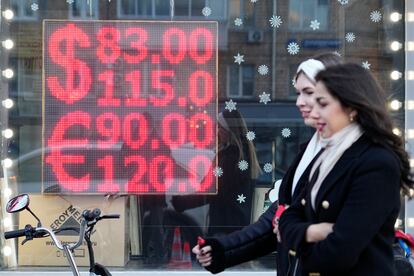 Ciudadanos rusos pasan al lado de una pantalla de una oficina de cambio de divisas que muestra los tipos de cambio del dólar estadounidense y el euro por rublos rusos en el centro de Moscú, Rusia.