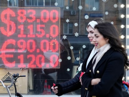 Ciudadanos rusos pasan al lado de una pantalla de una oficina de cambio de divisas que muestra los tipos de cambio del dólar estadounidense y el euro por rublos rusos en el centro de Moscú, Rusia.