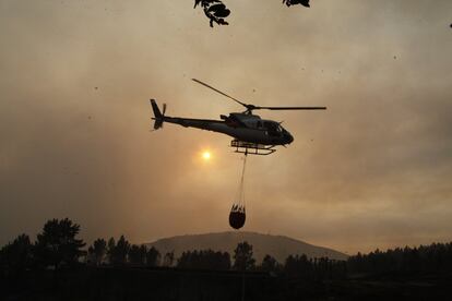 Un helicóptero transporta un depósito de agua hacia el incendio de Arbo (Pontevedra).