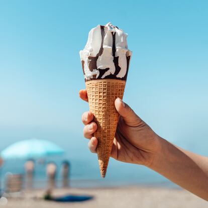 Cropped shot of woman hand holding ice-cream cone on the beach on a sunny day. Summer vacation concept.