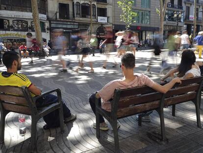 Diverses persones assegudes als bancs de la Rambla.