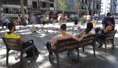 Diverses persones assegudes als bancs de la Rambla.