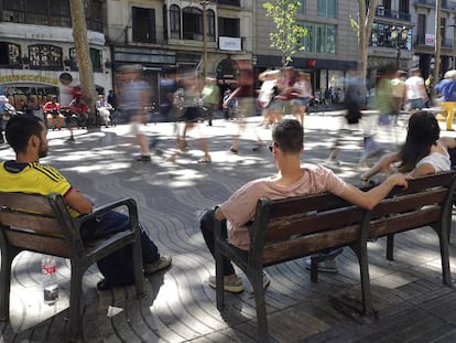 Varias personas sentadas en los bancos de La Rambla.