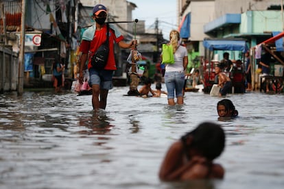 Un vendedor ambulante camina sobre el agua mientras los niños juegan en ella, en un área densamente poblada que se inunda debido a las mareas altas, en el distrito de Muara Angke en Yakarta, Indonesia, el pasado 9 de noviembre de 2021