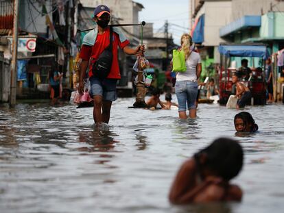 Un vendedor ambulante camina sobre el agua mientras los niños juegan en ella, en un área densamente poblada que se inunda debido a las mareas altas, en el distrito de Muara Angke en Yakarta, Indonesia, el pasado 9 de noviembre de 2021