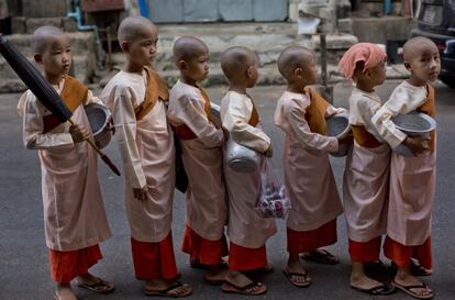 Monjes budistas novatos, esperan en fila delante de una casa para recoger limosna en Yangon (Myanmar).