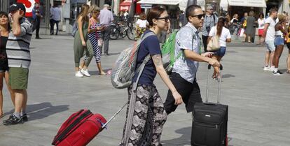 Dos turistas caminan con sus maletas en la Puerta del Sol.