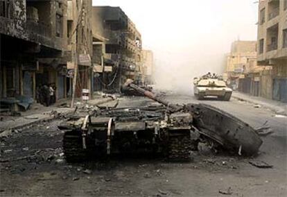 Un carro de combate iraquí, destruido en una calle de Bagdad por la que pasa un blindado estadounidense.
