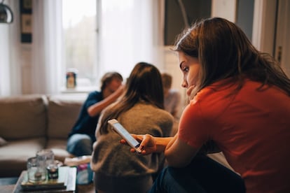 Girl using smart phone while sitting with friends in living room