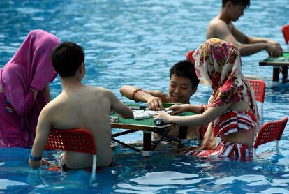 Varias personas juegan al mahjong en una piscina durante una alerta roja por temperaturas en Chongqing, en el sur de China.