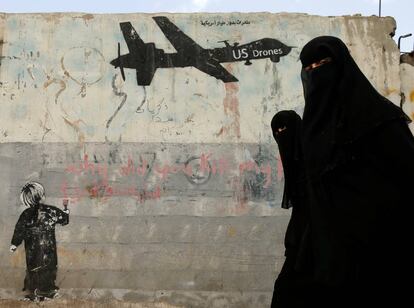 Dos mujeres pasan delante de un graffiti, que denuncia los bombardeos con drones sobre Yemen, en una pared de Saná.